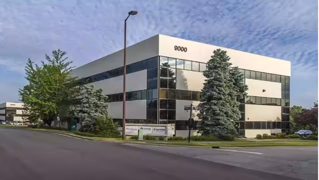 Exterior of a modern glass-front building with trees and a street in front