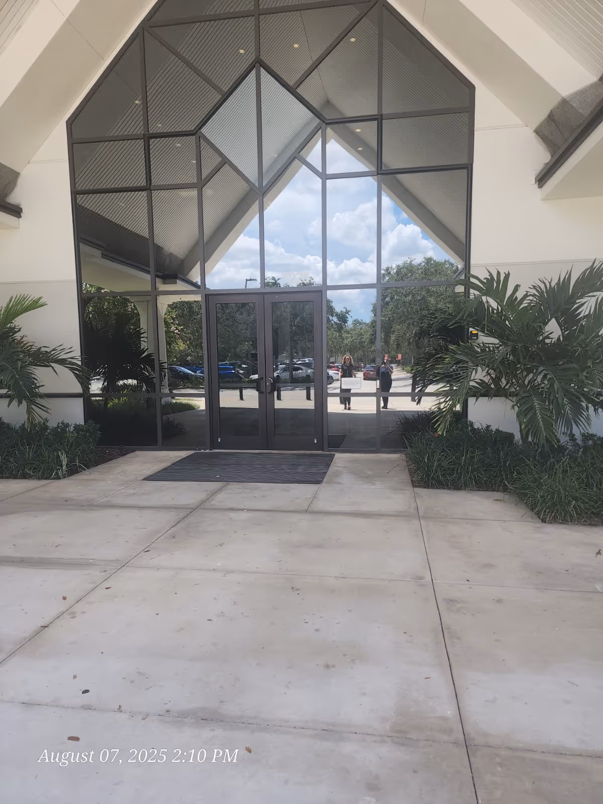 Modern facility entrance with glass doors and reflections of people outside.