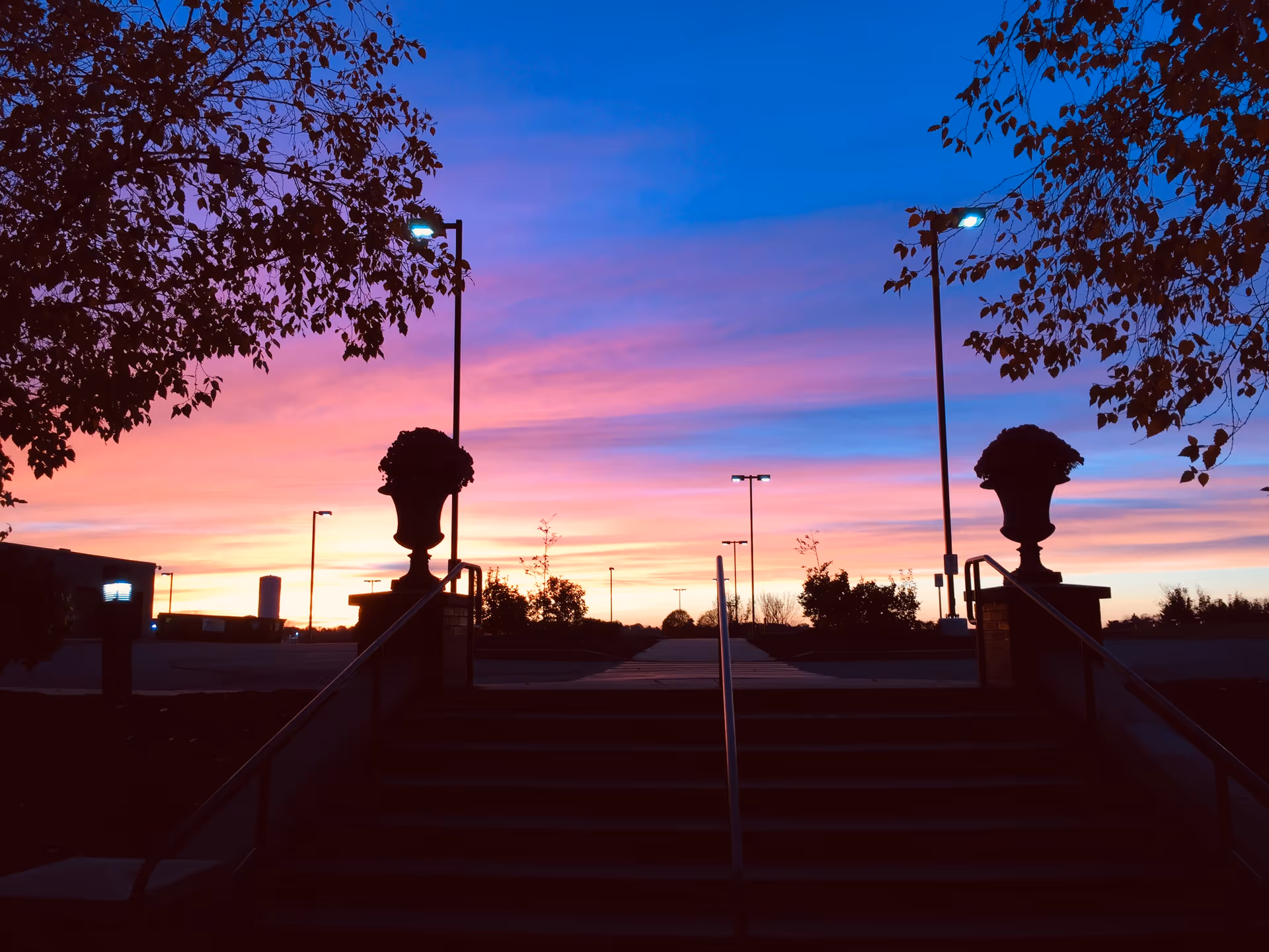 Silhouetted steps and urns lead to a building entrance at sunset.
