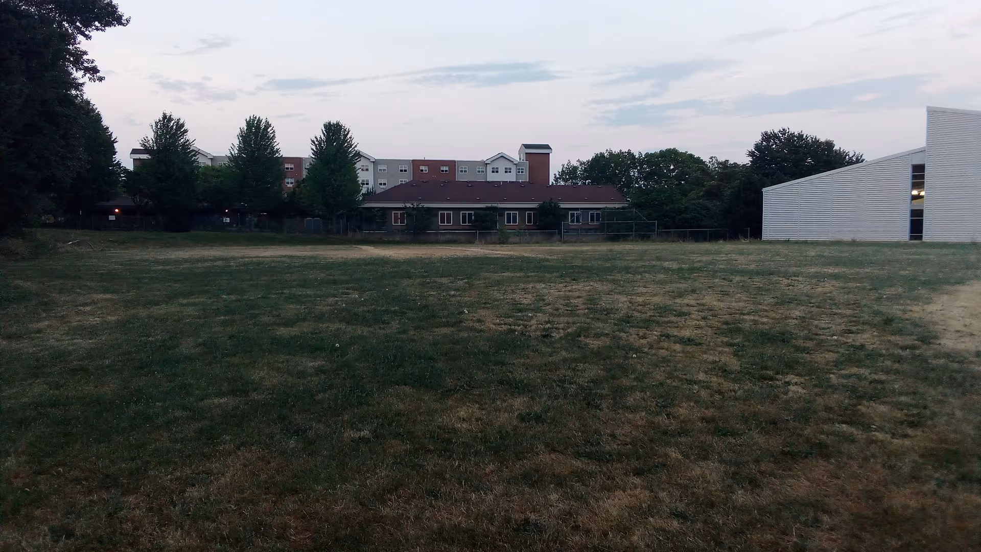 Open grassy field with trees and distant facility buildings.