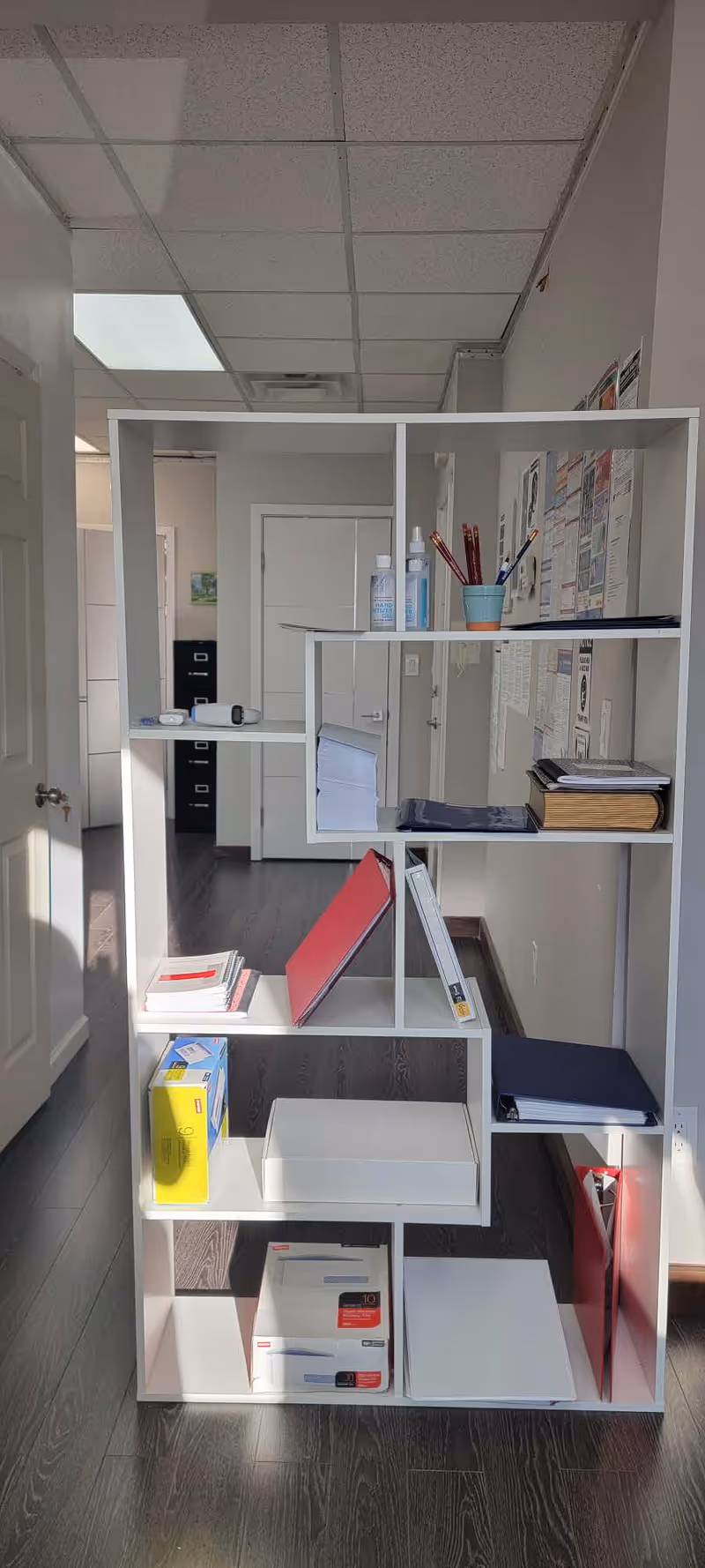 White modular shelving unit filled with files and supplies in a hallway.