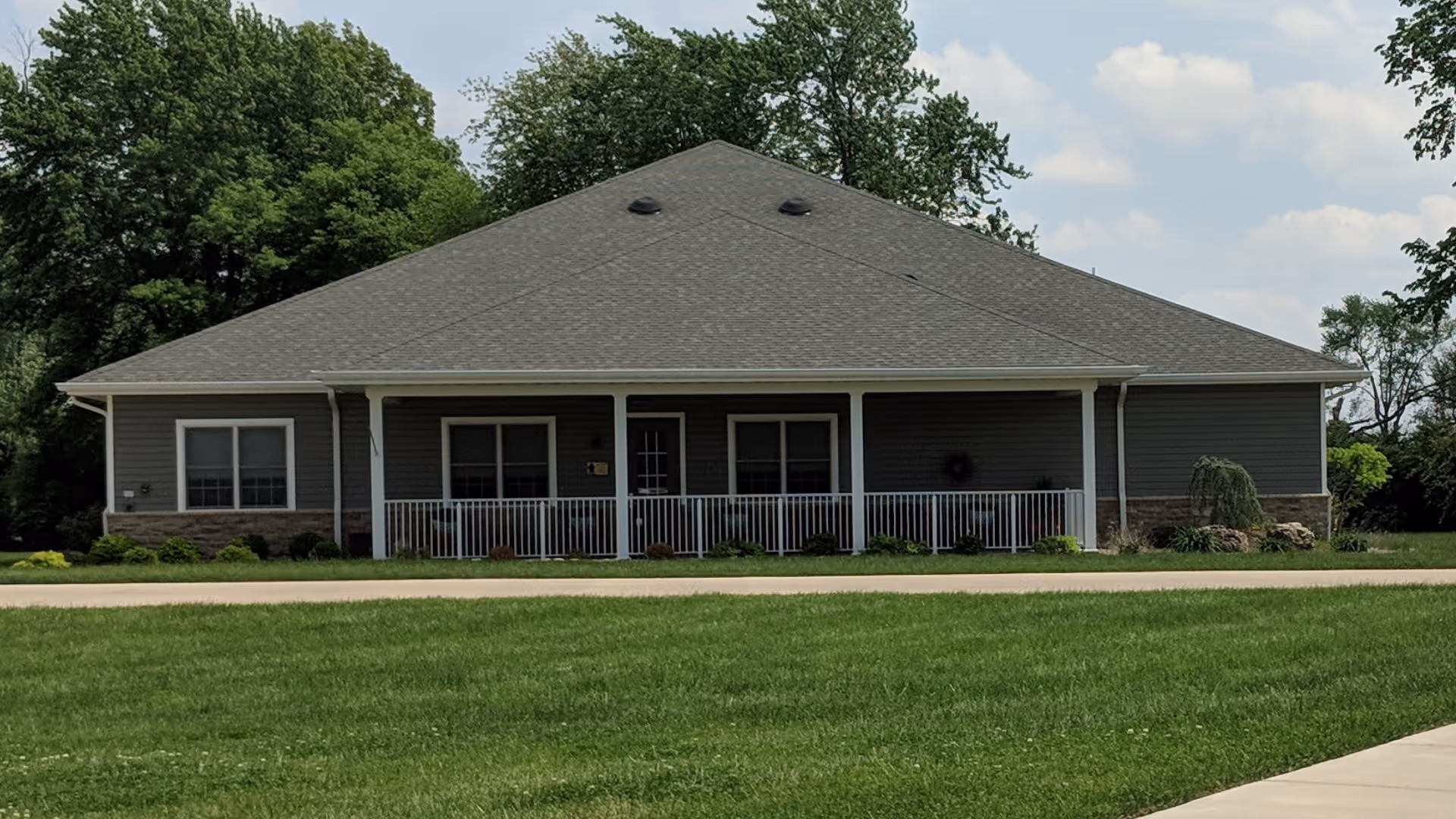 Single-story gray building with a wide front porch and green lawn.
