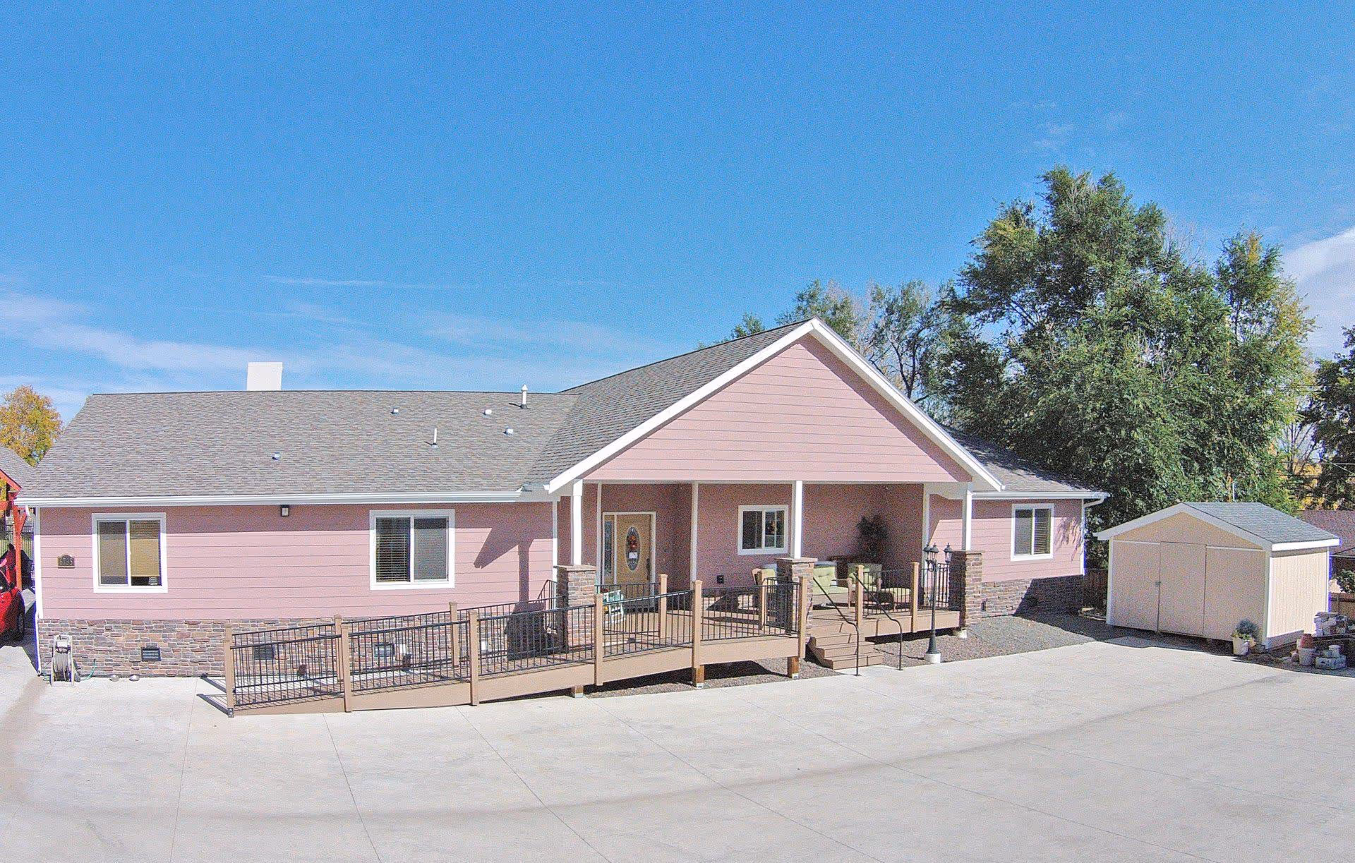 Single-story pink senior living residence with a ramped front porch and nearby shed.