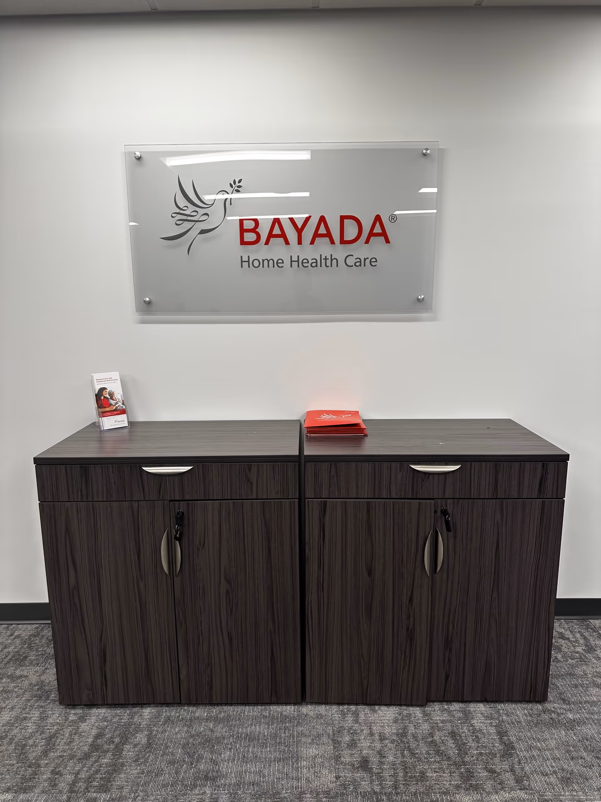 Two dark wood cabinets beneath a BAYADA Home Health Care sign in a hallway.