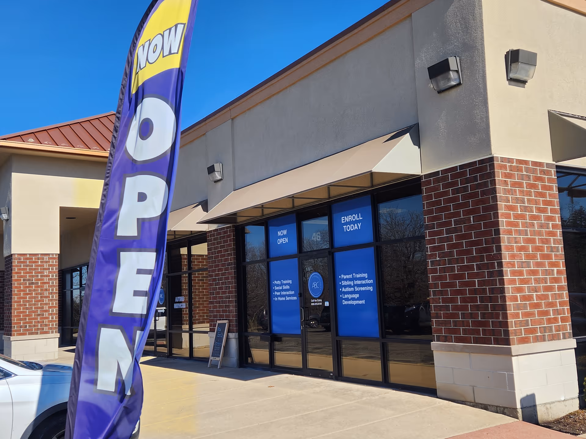 Exterior of a facility with a tall purple OPEN flag and blue entrance signs.