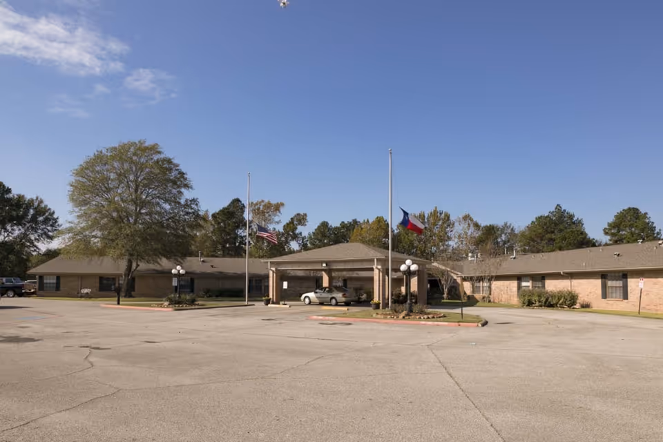 Exterior view of a single-story brick senior facility with flagpoles and a covered entrance.