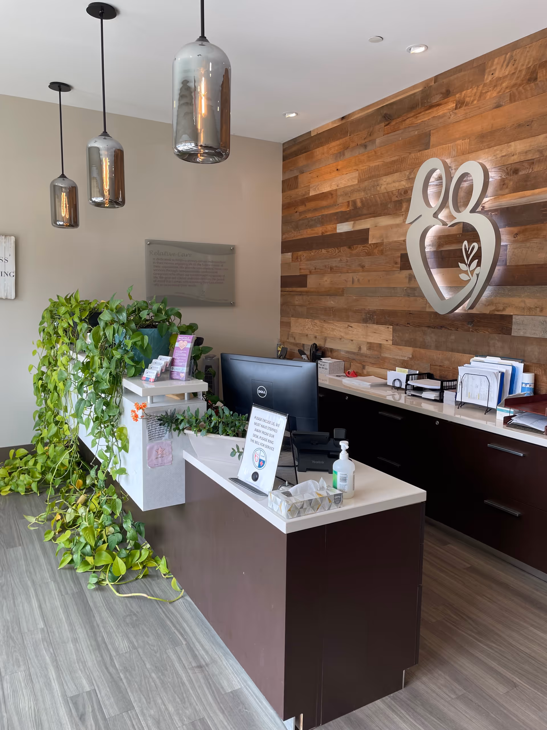 Reception area inside a senior living facility with wood wall and plants.