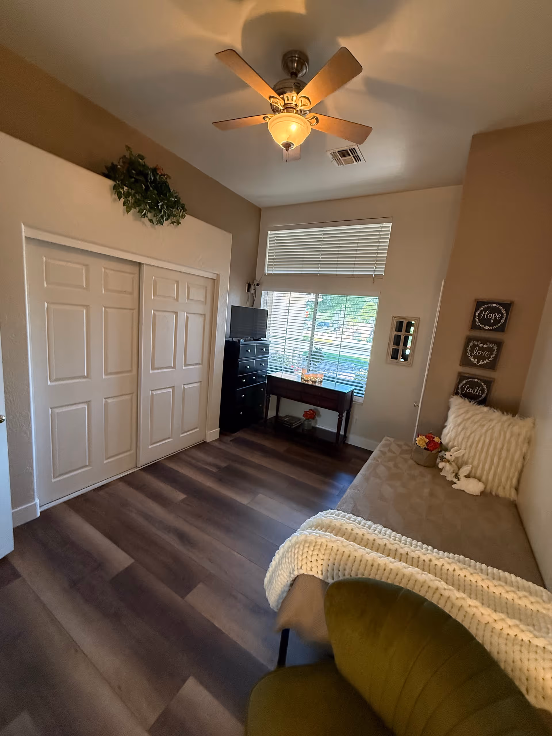 Cozy senior living bedroom with daybed, ceiling fan, dresser, and window blinds.