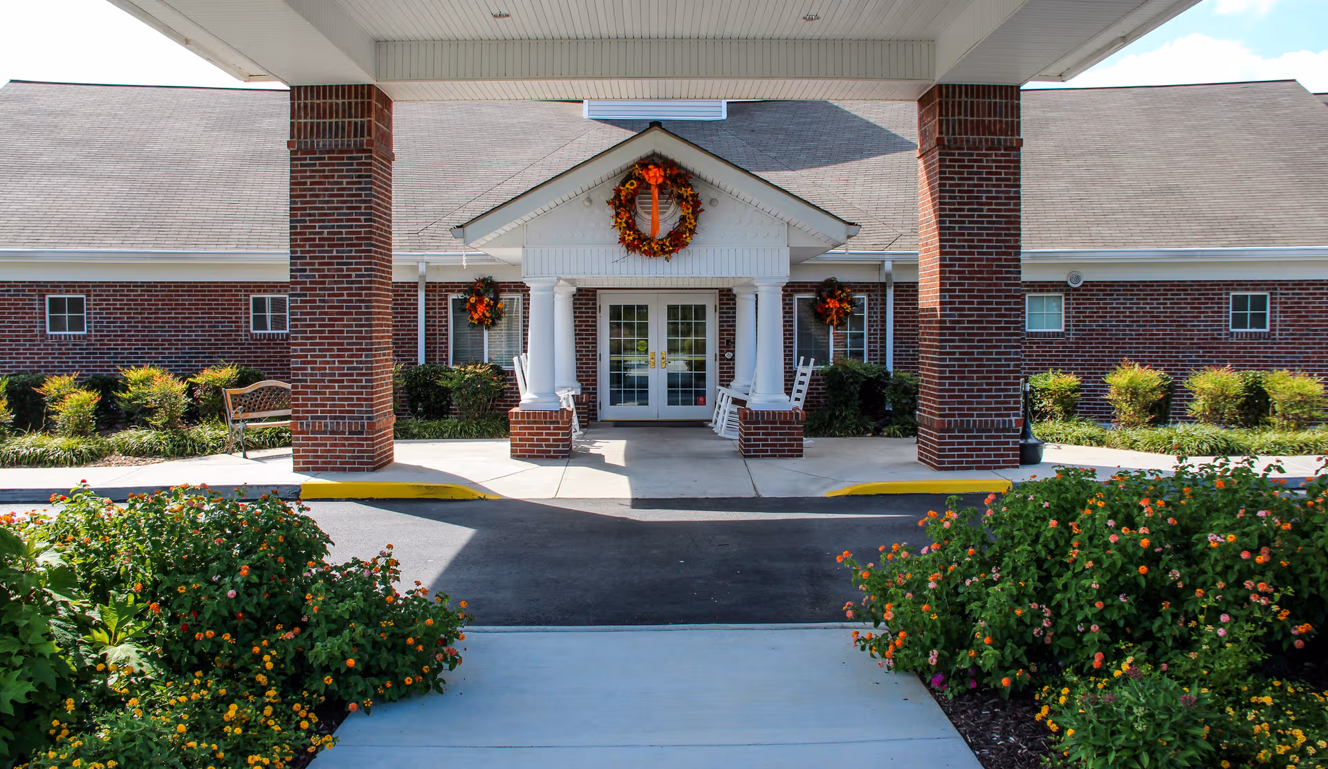 Front entrance of a brick senior living facility with wreaths and landscaped flowers.