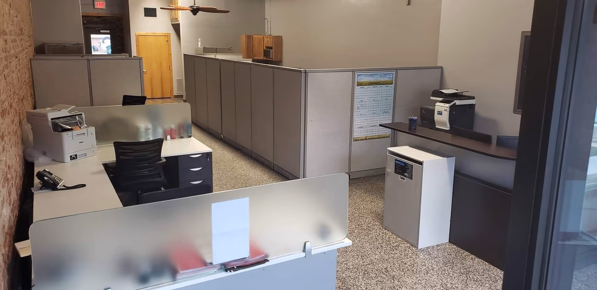 Office area with cubicles, desks, printer, and a reception counter in a hospice facility