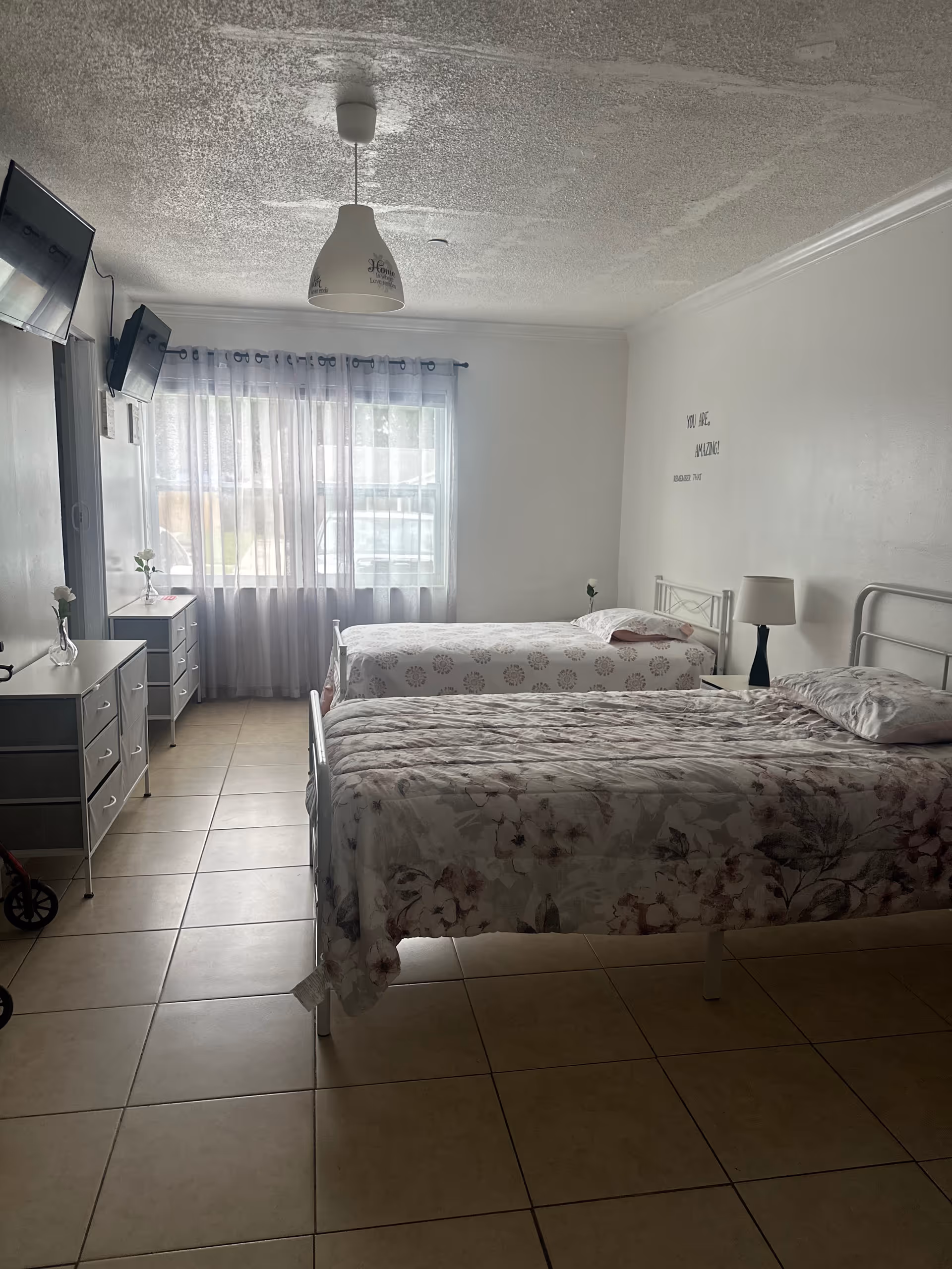 Two metal beds with matching dressers and a large window in a bright bedroom.