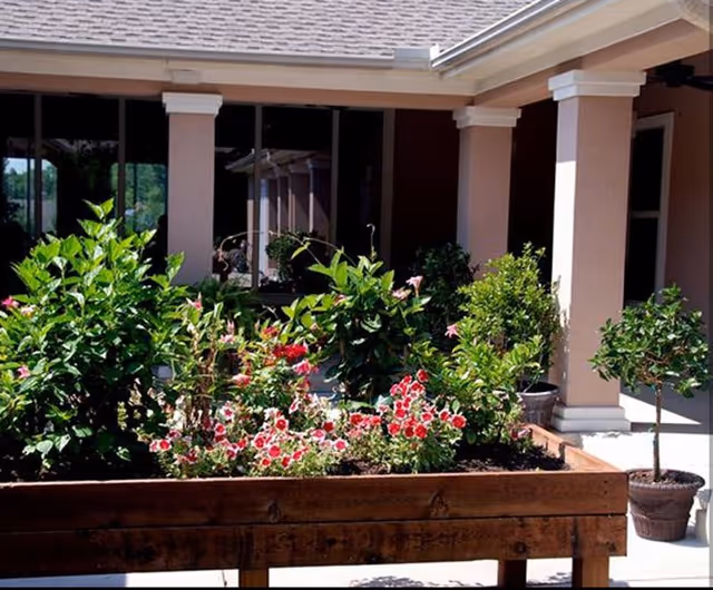 Front exterior of a care home with pink columns and lush flower beds.