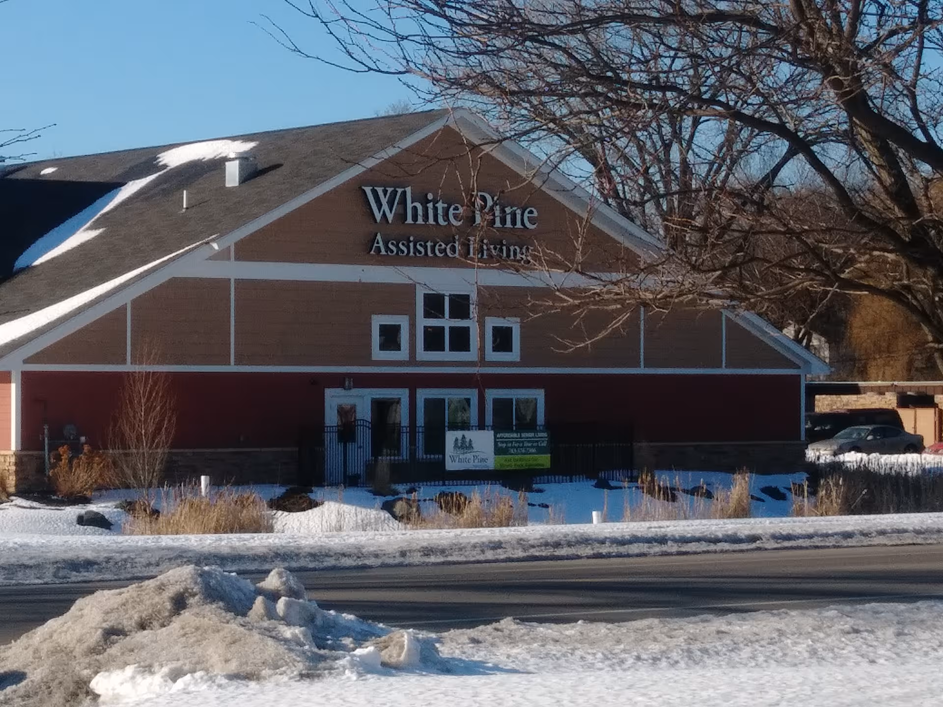 Exterior view of White Pine Assisted Living building with snow-covered ground and bare trees.