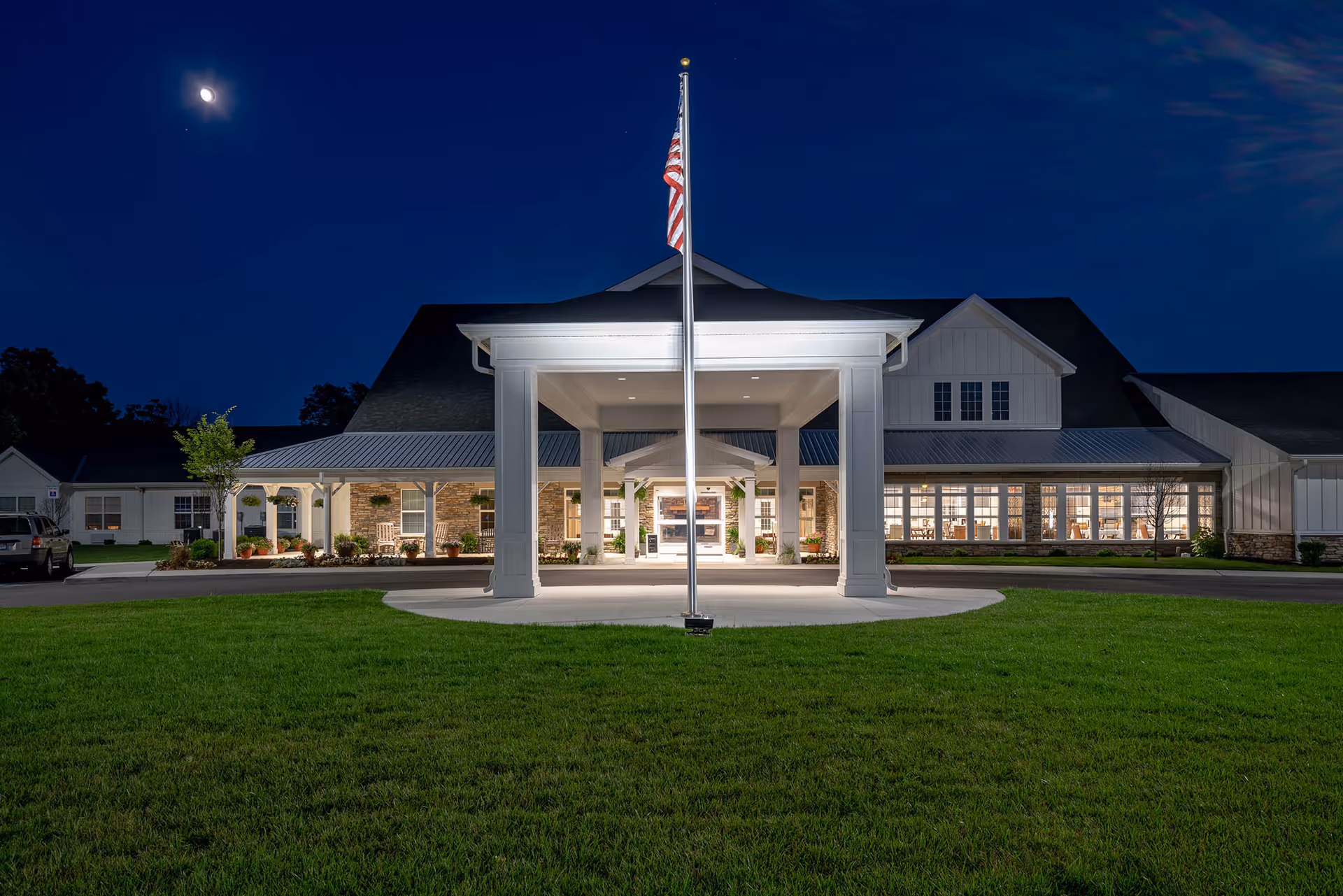 Night exterior of Demaree Crossing facility with lit entrance canopy and flag.