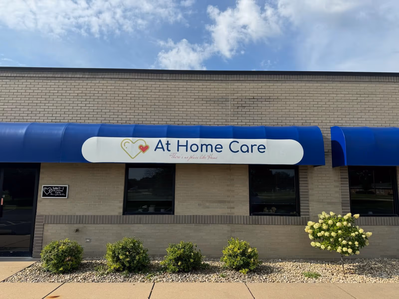 Brick facility storefront with blue awning and At Home Care sign across the front.
