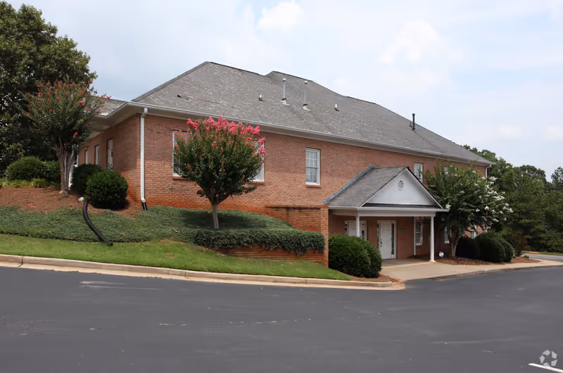 Brick senior living facility exterior with entry portico, landscaped shrubs, and trees.