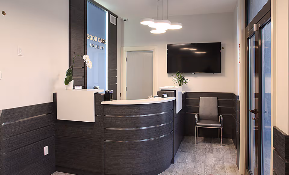 Modern reception area featuring curved dark wood desk, plants, and a wall-mounted TV.