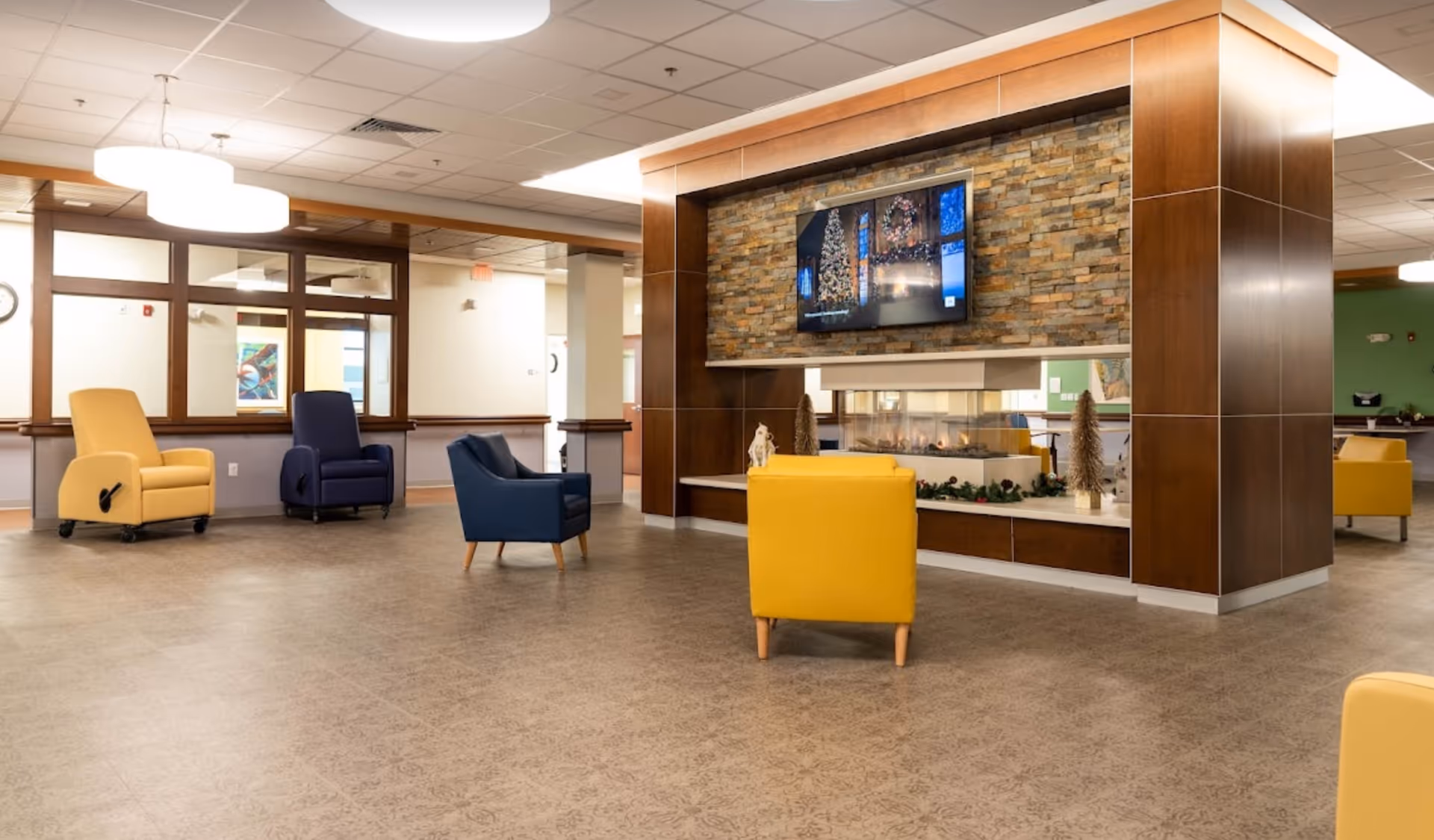 Spacious modern senior living lobby with colorful chairs, a stone fireplace, and a TV.