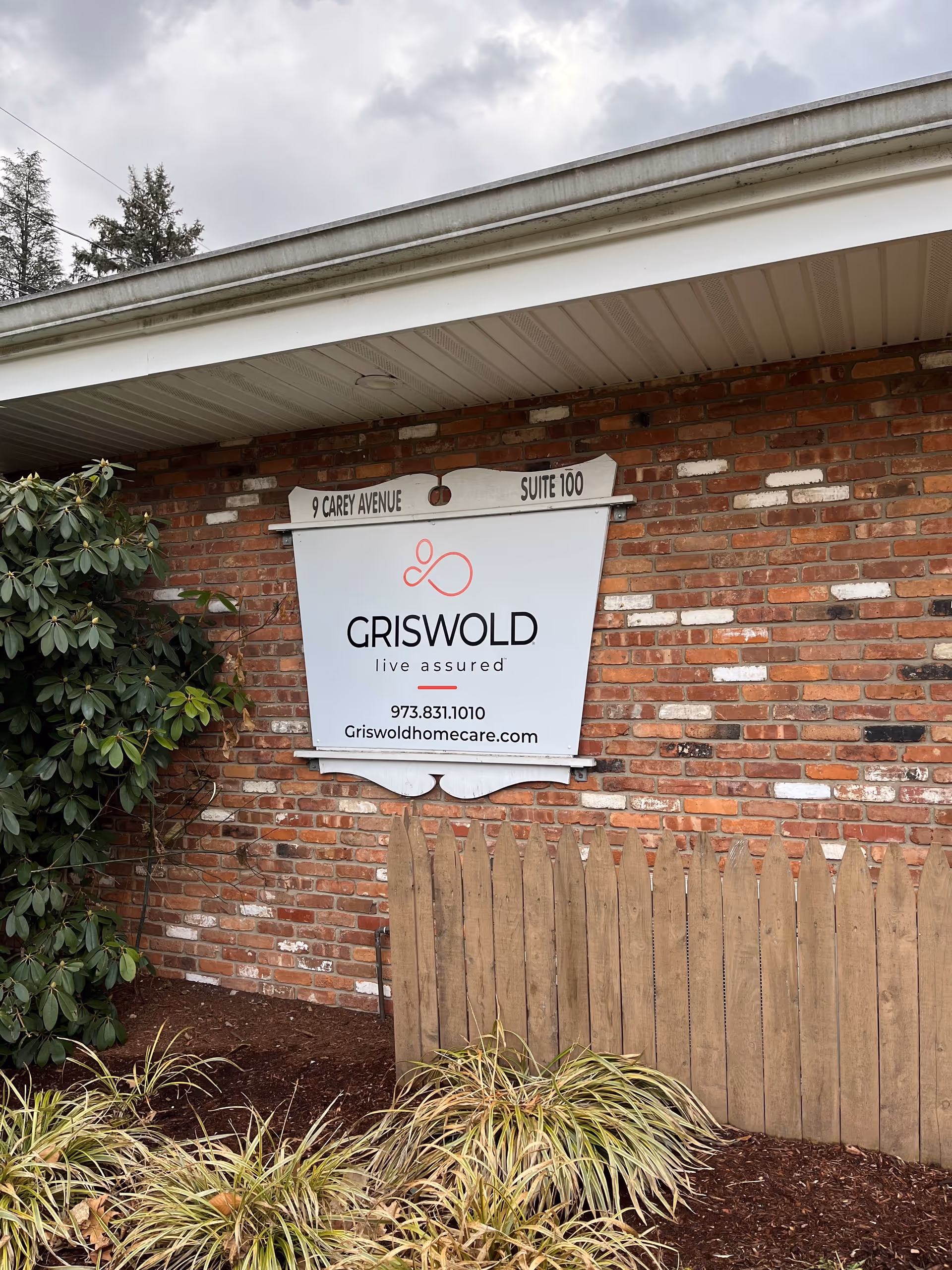 Exterior brick wall with Griswold Home Care sign and surrounding plants