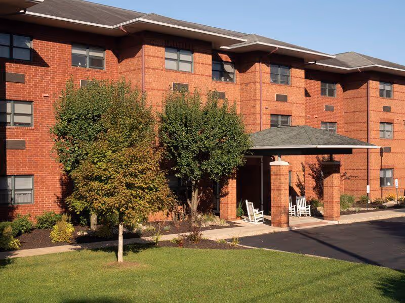 Red brick senior living building exterior with entrance porch and trees.