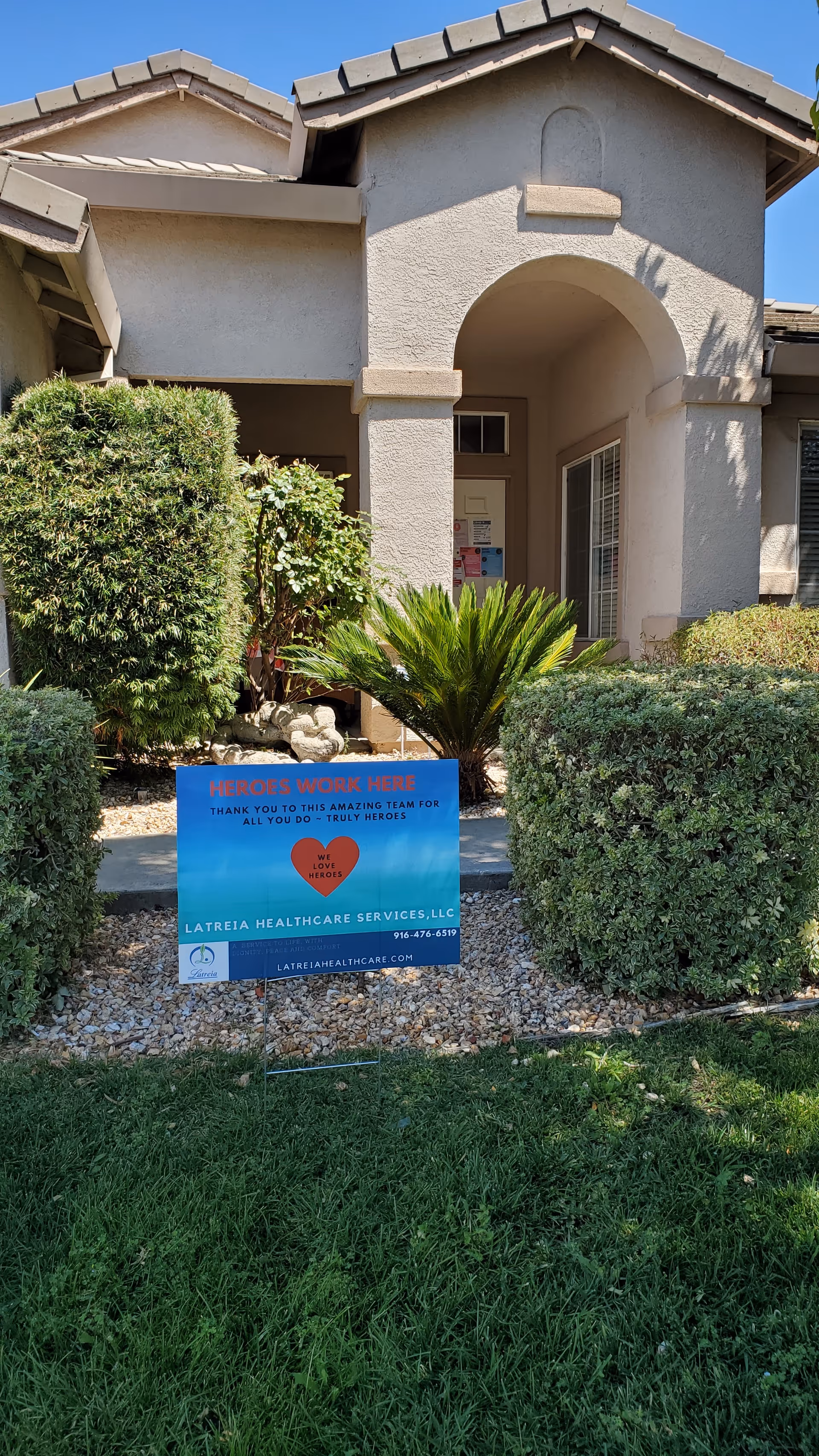 Beige assisted living facility entrance with archway and a landscaping sign.