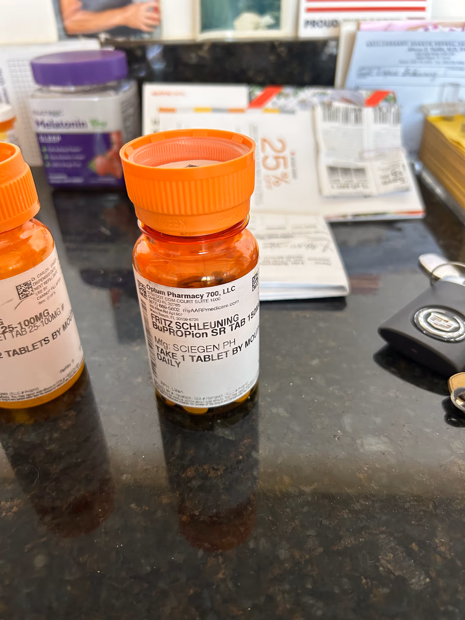 Close up of orange prescription bottles on a dark countertop with paperwork in background.