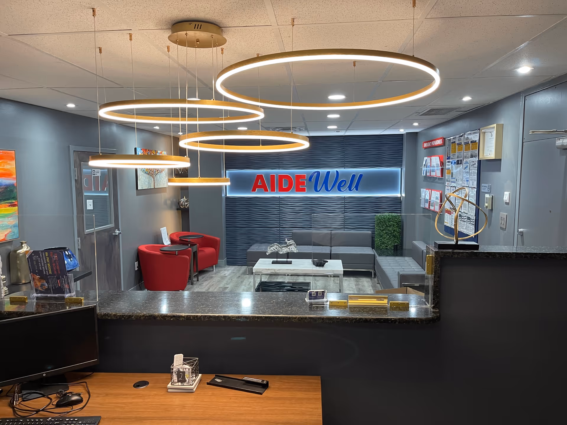 Reception lobby with circular pendant lights, gray seating, and an AIDEWell sign.