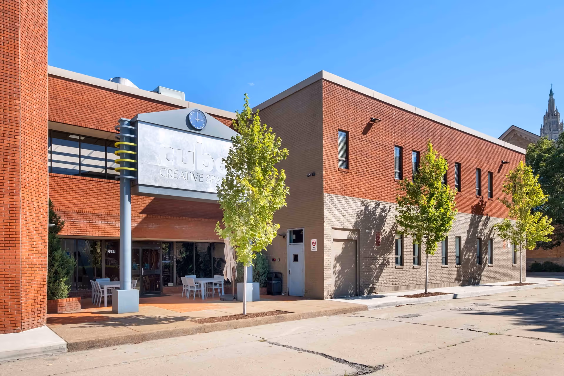 Brick building exterior with outdoor seating and a storefront sign under blue sky.