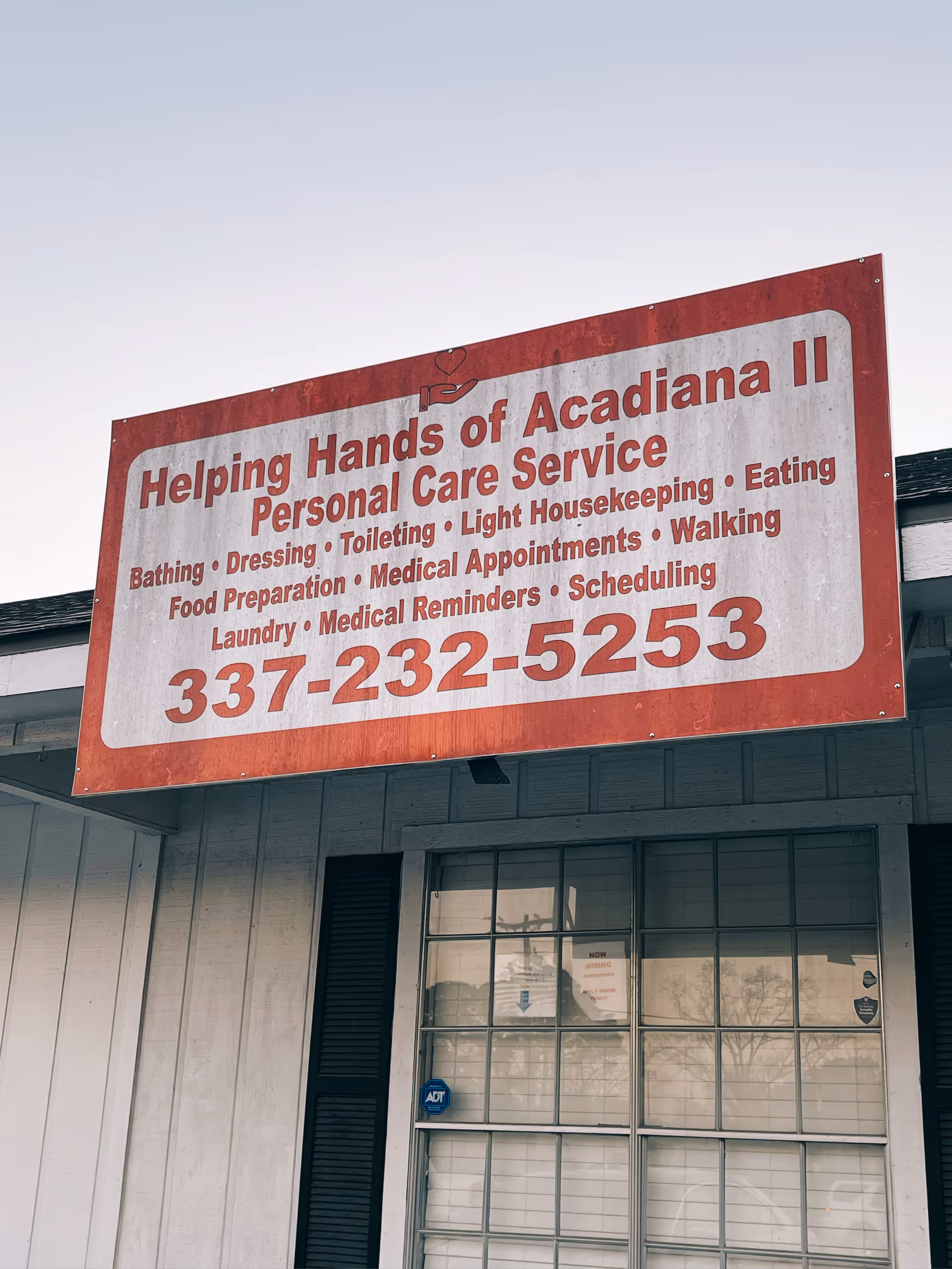 A large red and white sign for Helping Hands of Acadiana II on a building exterior.