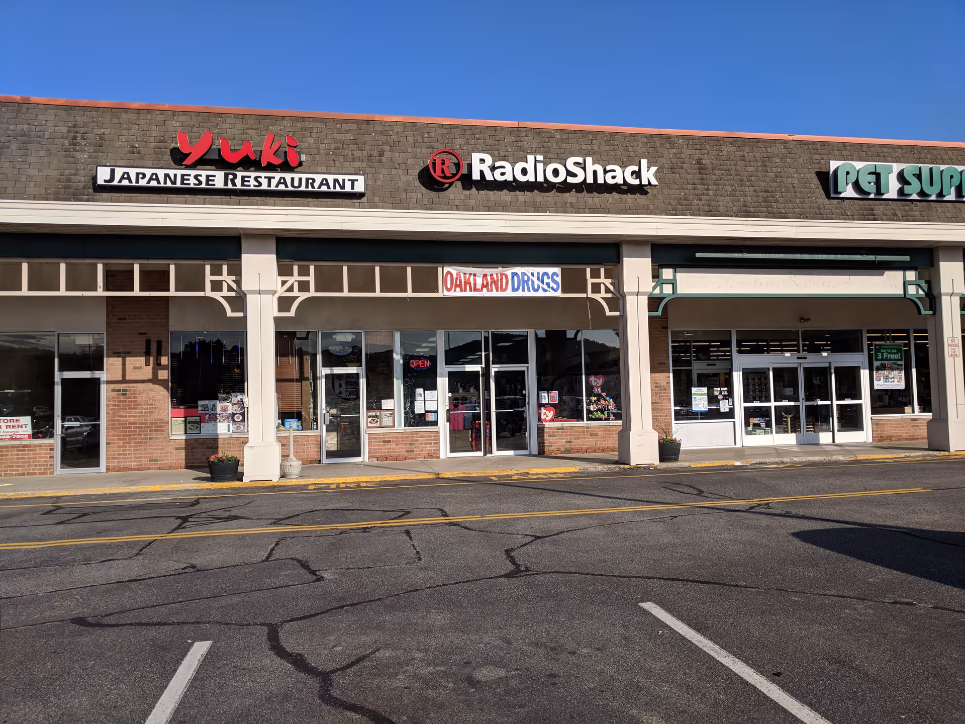 Facade of a strip mall with Yuki Japanese Restaurant, RadioShack, and Oakland Drugs signs.