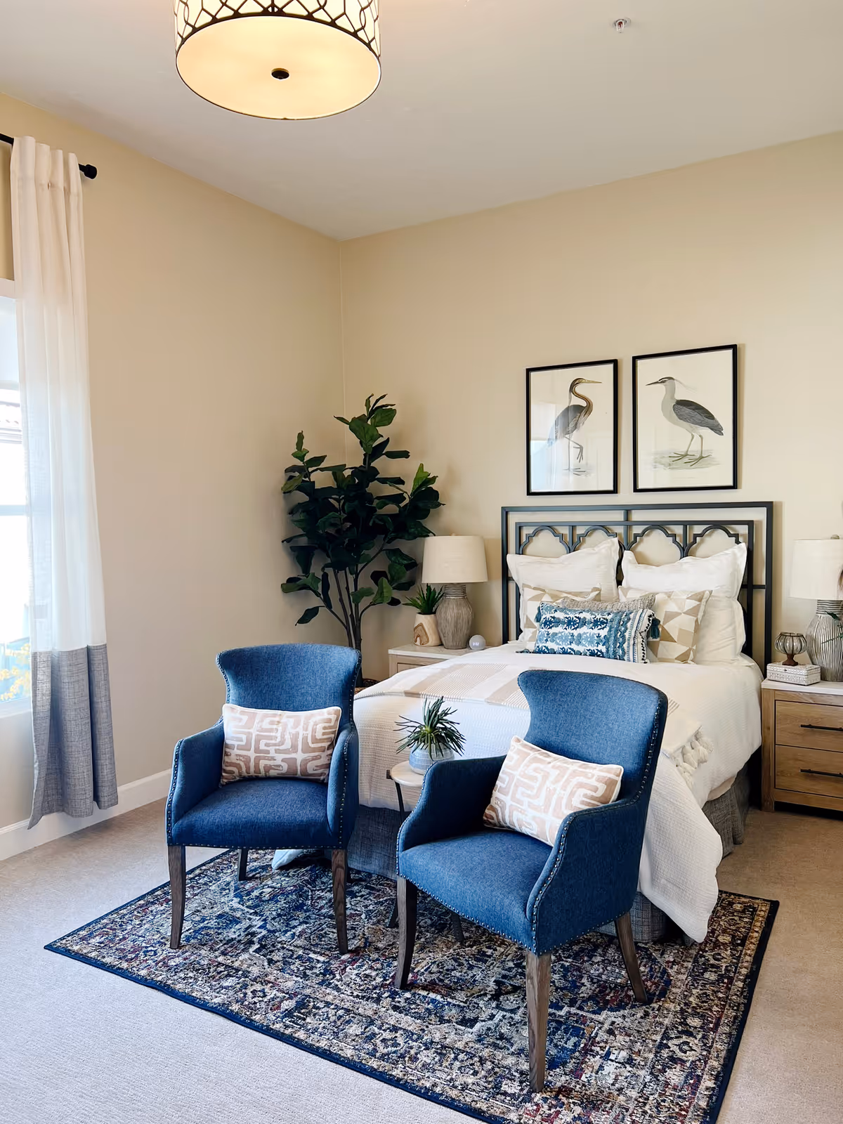 Cozy bedroom in a senior facility with two blue chairs, bed, pillows, and plants.