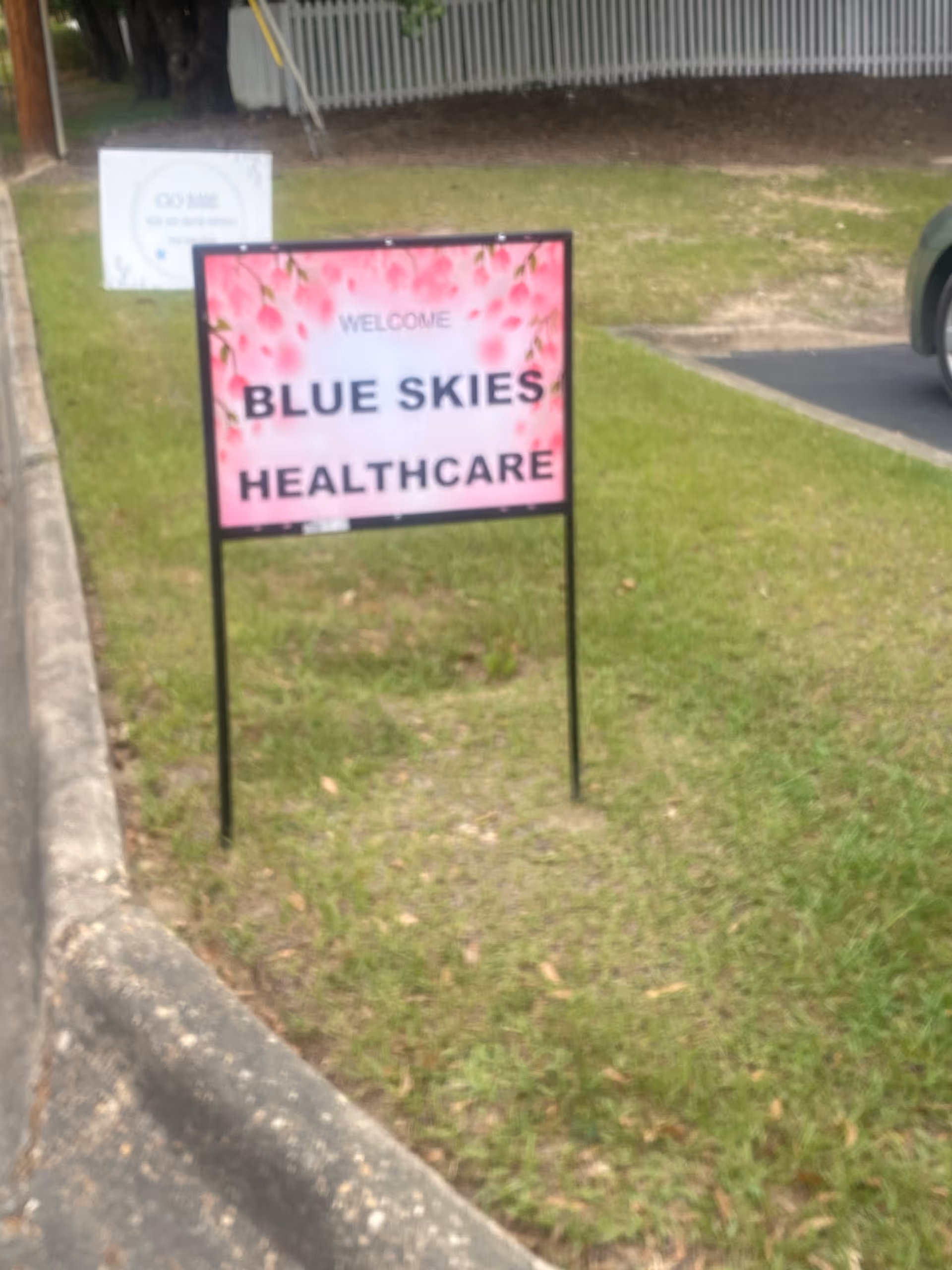 Pink welcome sign reads Blue Skies Healthcare on a grassy front lawn.