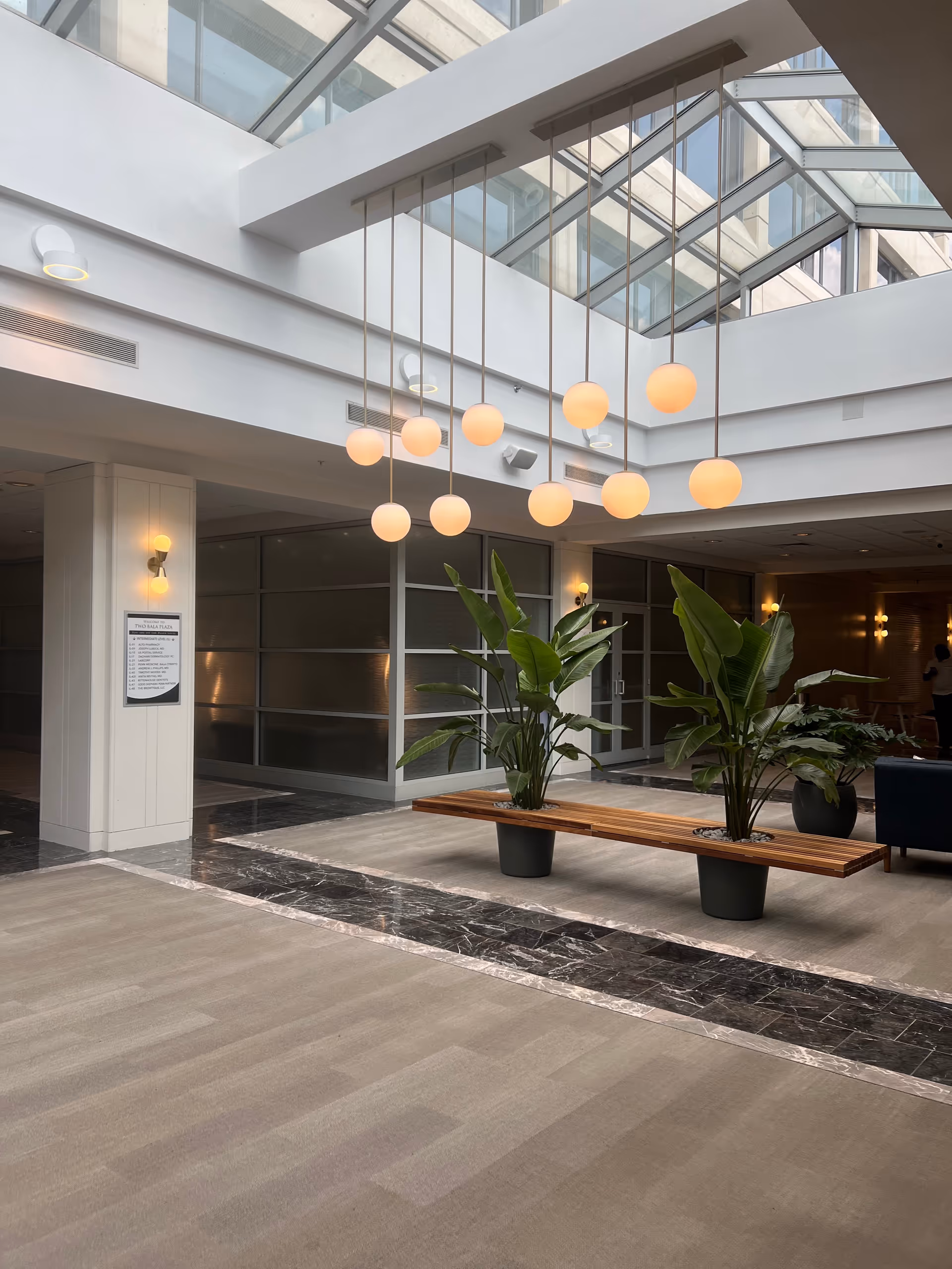 Bright indoor atrium lobby with hanging globe lights, benches, and large potted plants.