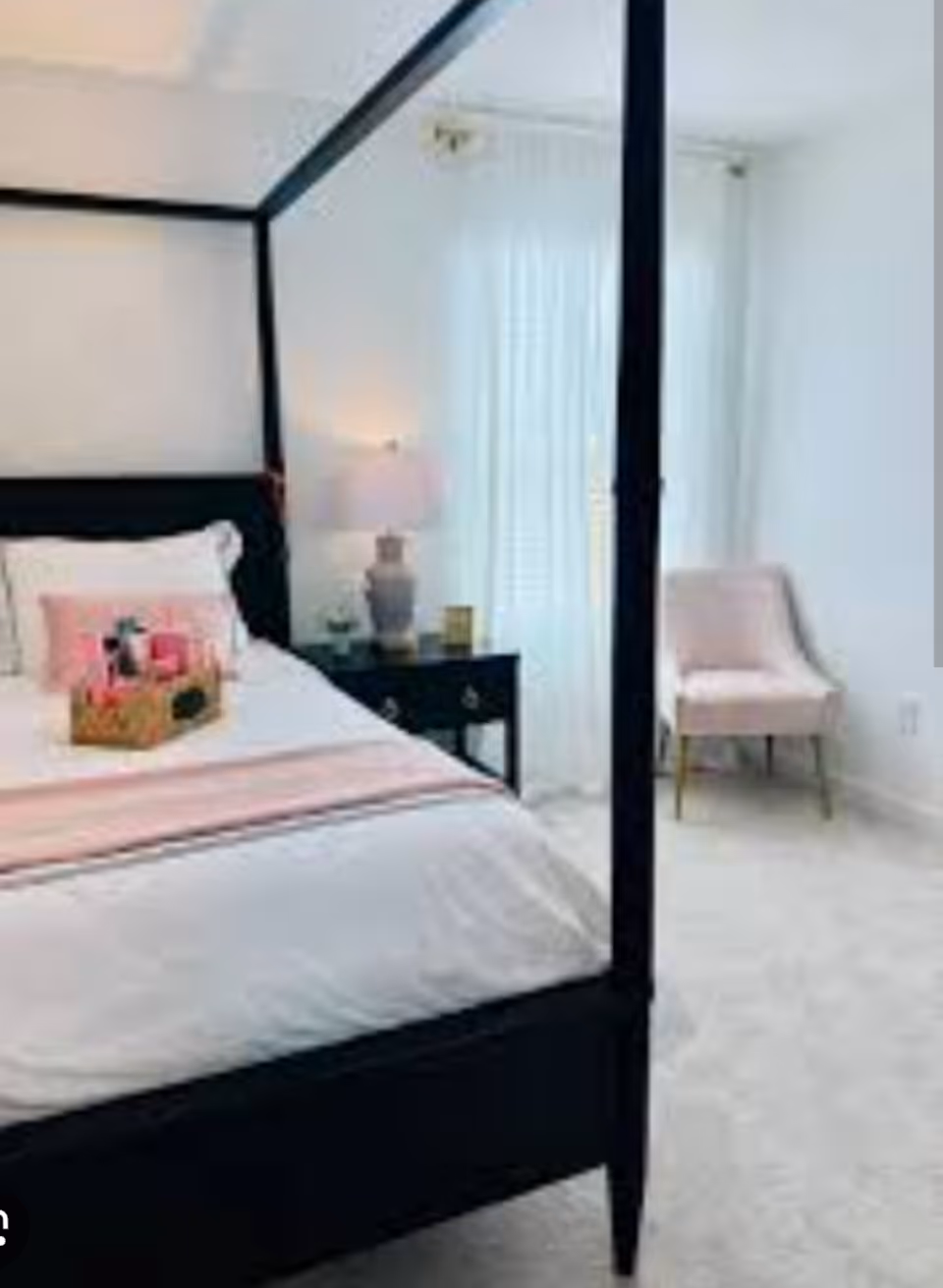 A four-poster bed with white and pink bedding in a bright bedroom.