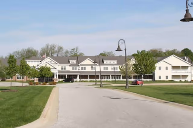 Front exterior view of Hamilton Grove senior living facility with driveway, lawn, and street lamps.