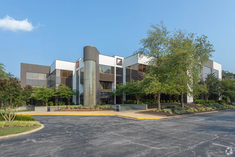 Modern senior care facility exterior with trees, landscaping, and a parking lot.