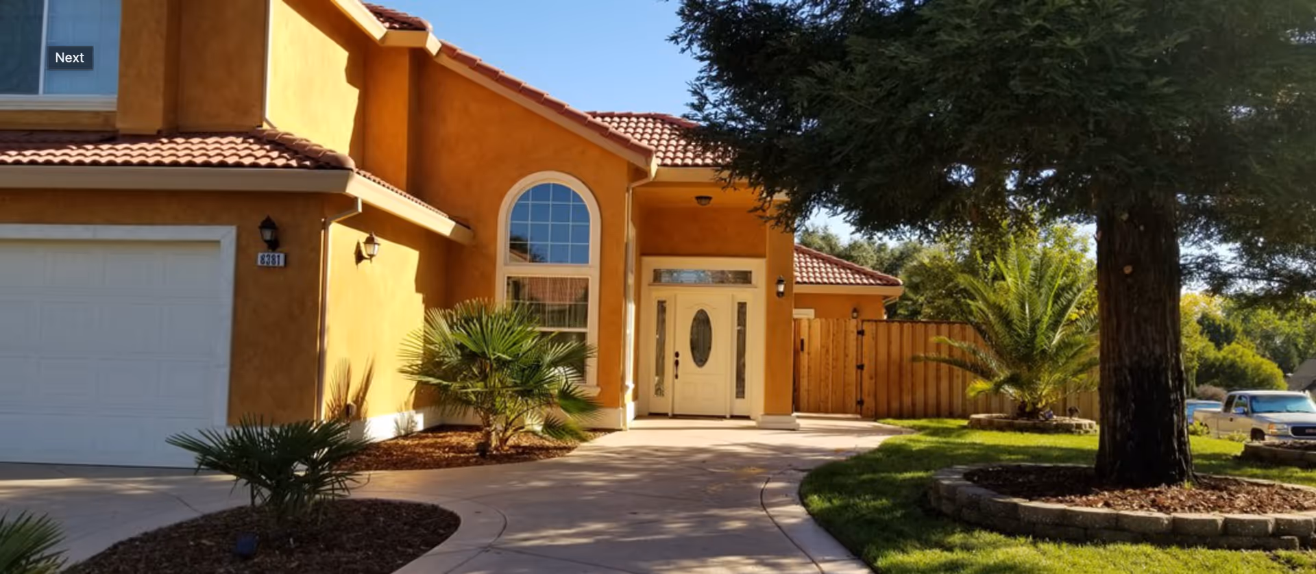 Front exterior of a stucco house with a tiled roof, driveway, garage and landscaped yard.