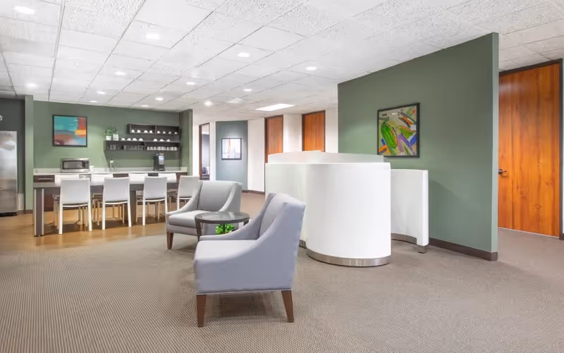 Modern senior living facility lobby with seating, reception desk, kitchenette, and soft green walls.