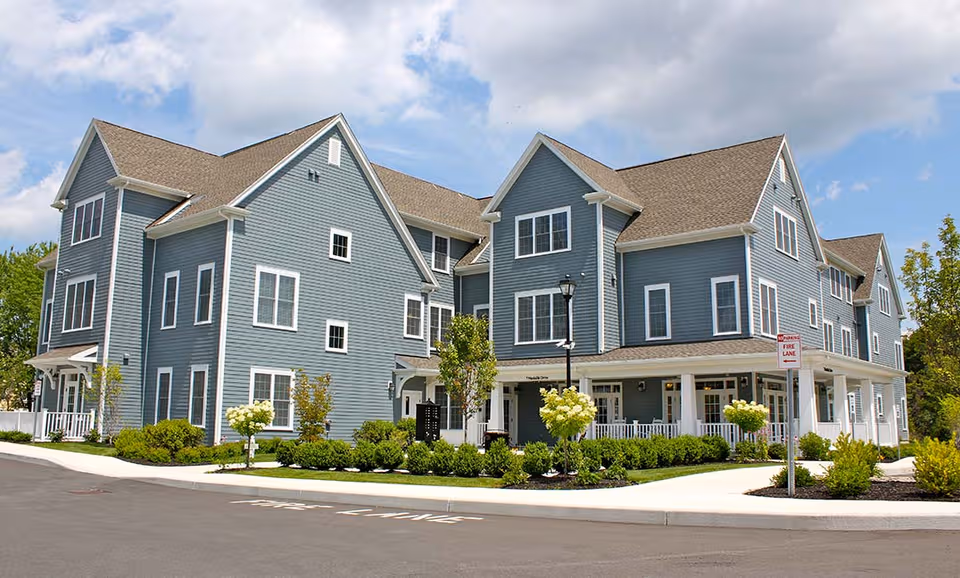Blue multi-wing senior living building with white trim, porches, and manicured landscaping.
