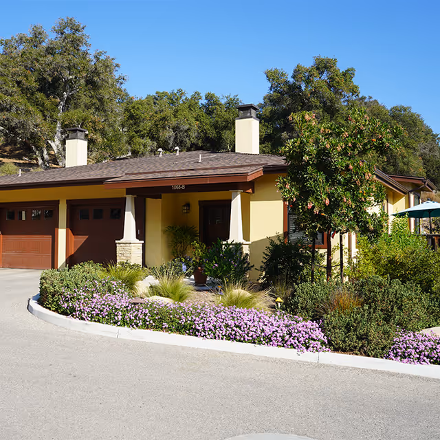 Front exterior of a single-story building with a two-car garage, porch, and landscaped flowerbeds.