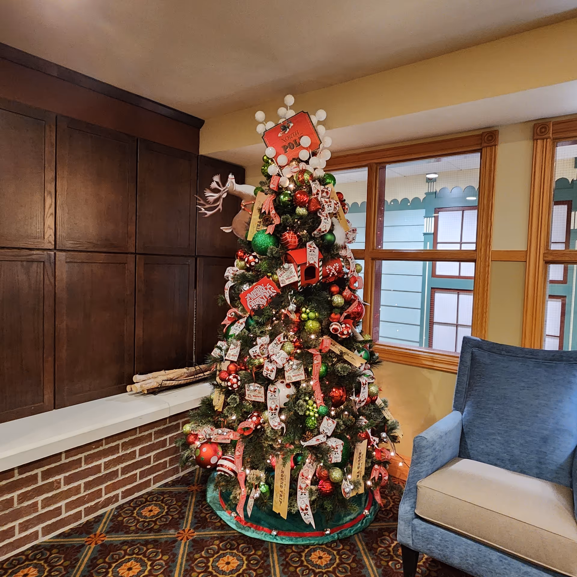 Decorated Christmas tree stands beside a blue chair in a cozy facility lobby.