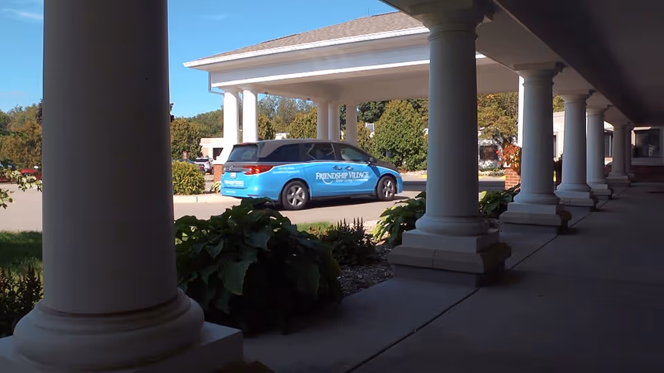 Blue Friendship Village car parked along a colonnade outside the facility.
