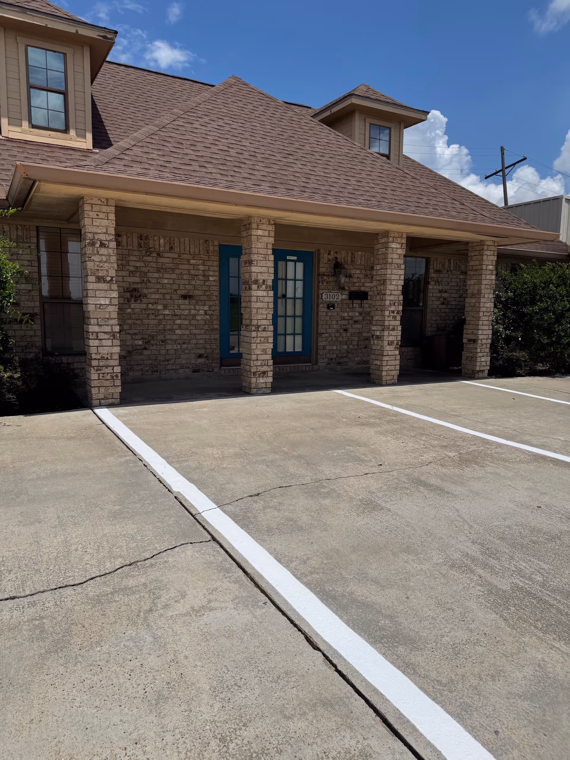 Brick-clad facility entrance with blue doors, columns, and a parking lot in front.