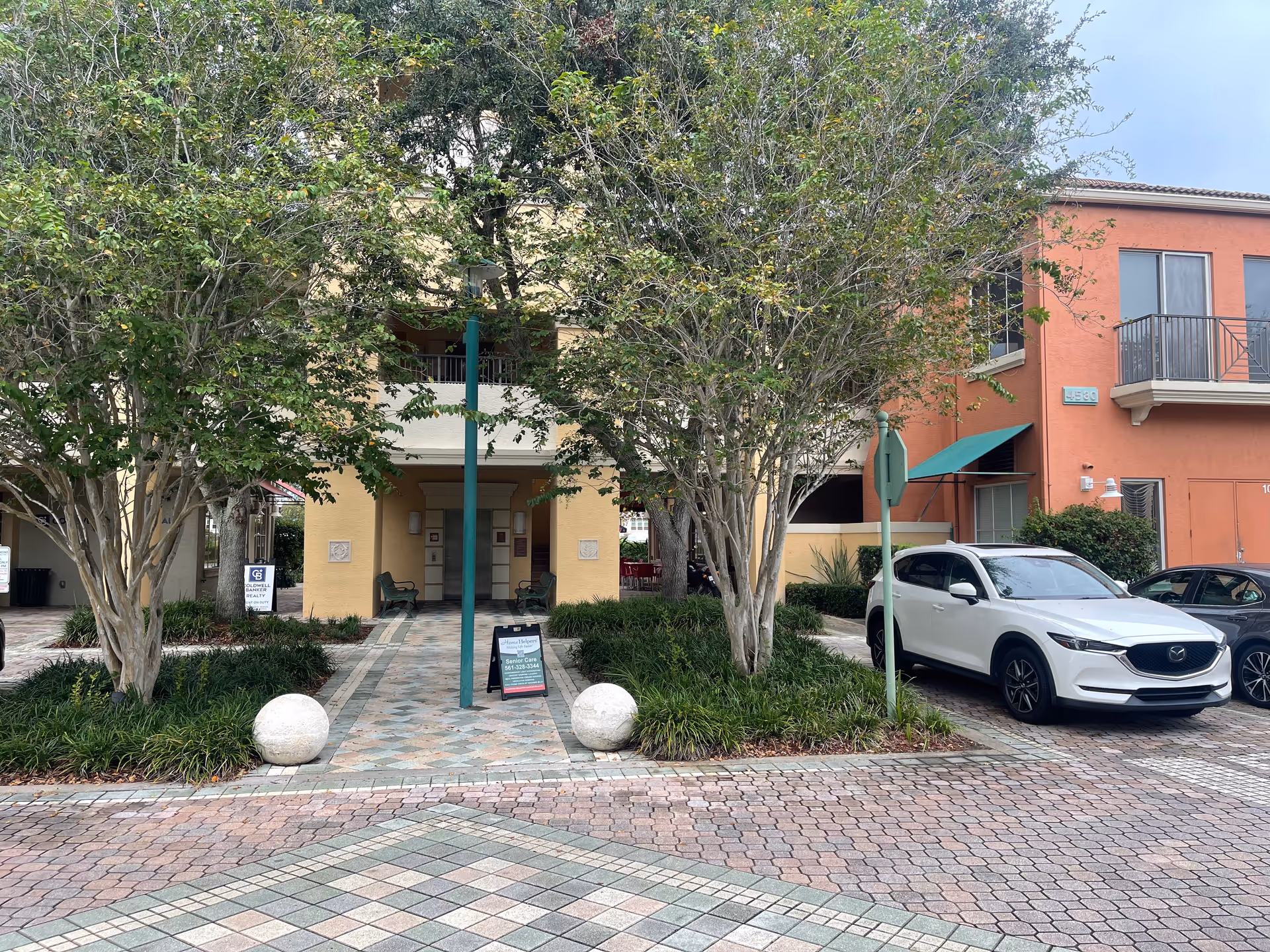 Exterior view of Home Helpers senior living building with courtyard and parked white car.