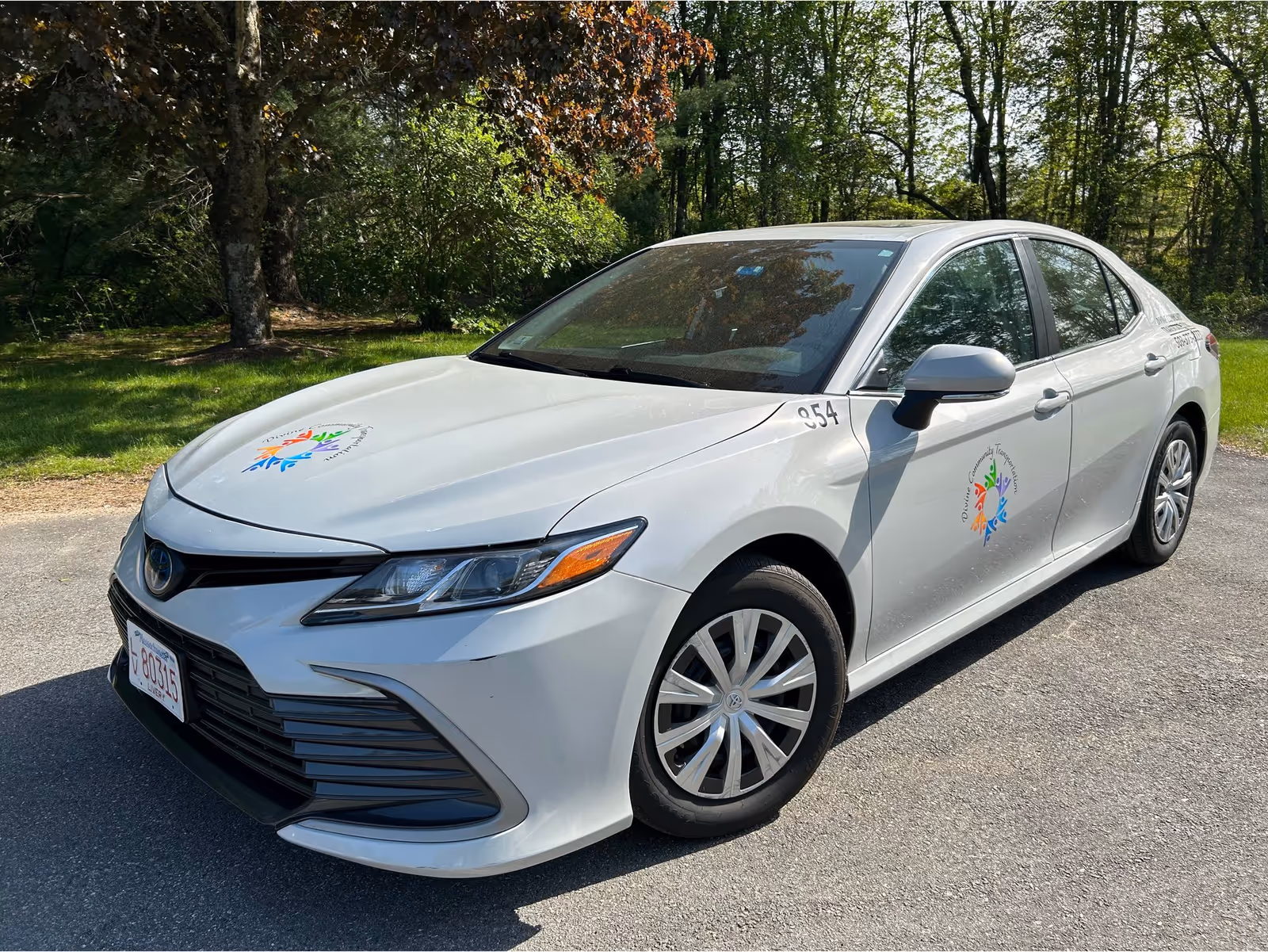 White sedan with colorful logos parked on a tree-lined road