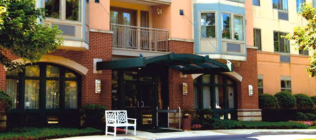 Exterior view of Leisure Park senior living building with brick facade, awnings, and a white bench.
