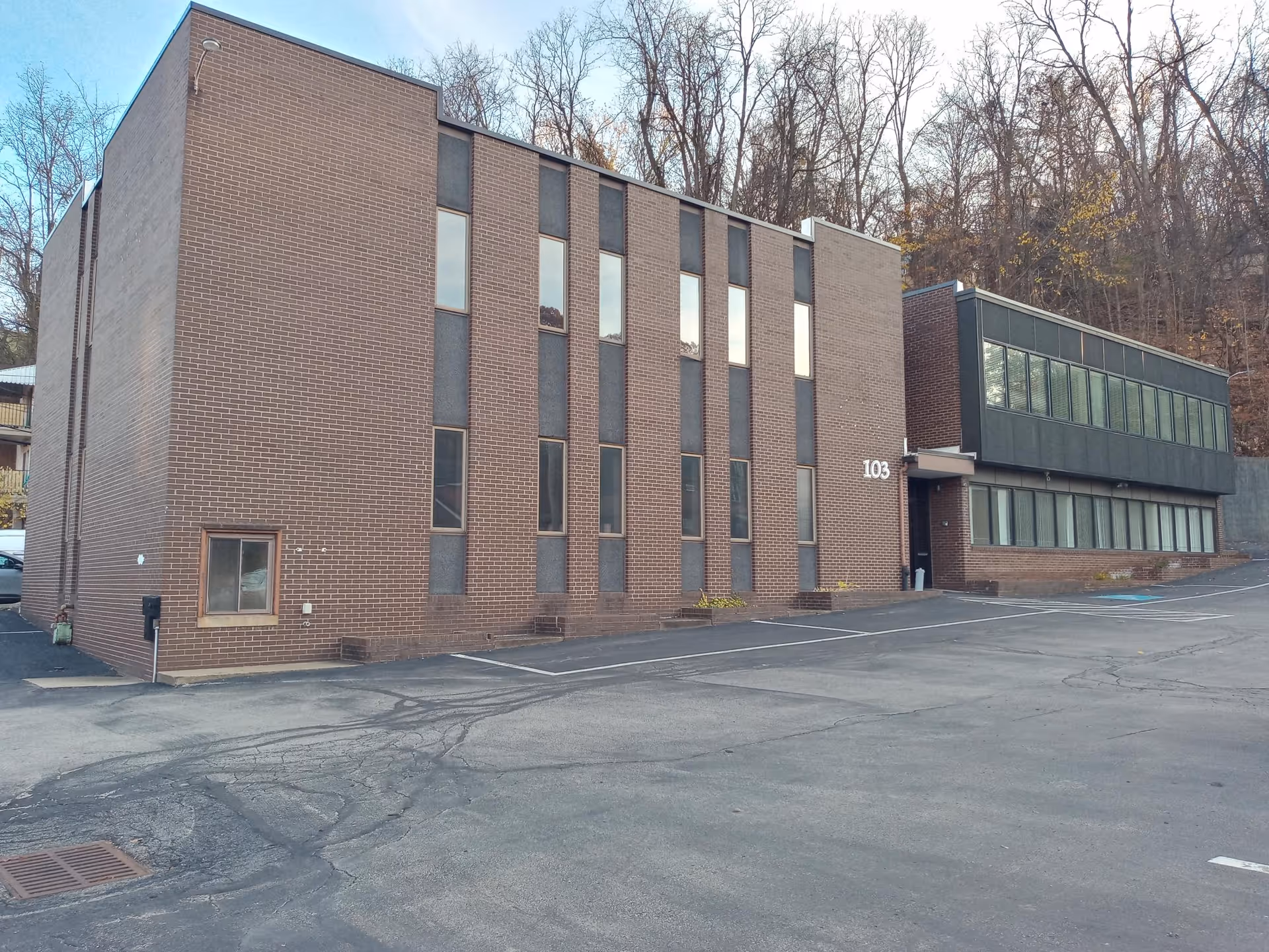 Brick exterior of a multi-story facility with windows, parking lot, and trees.