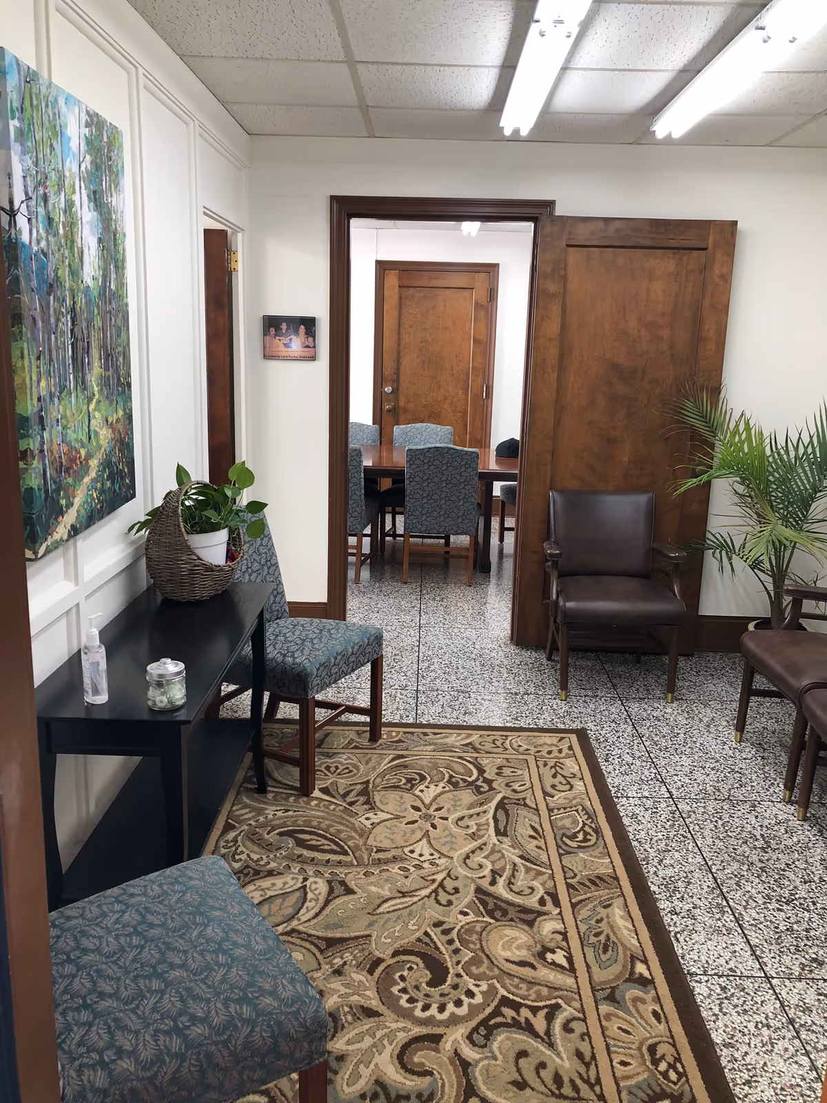 A waiting area in a senior facility with chairs, plants, and a decorative rug