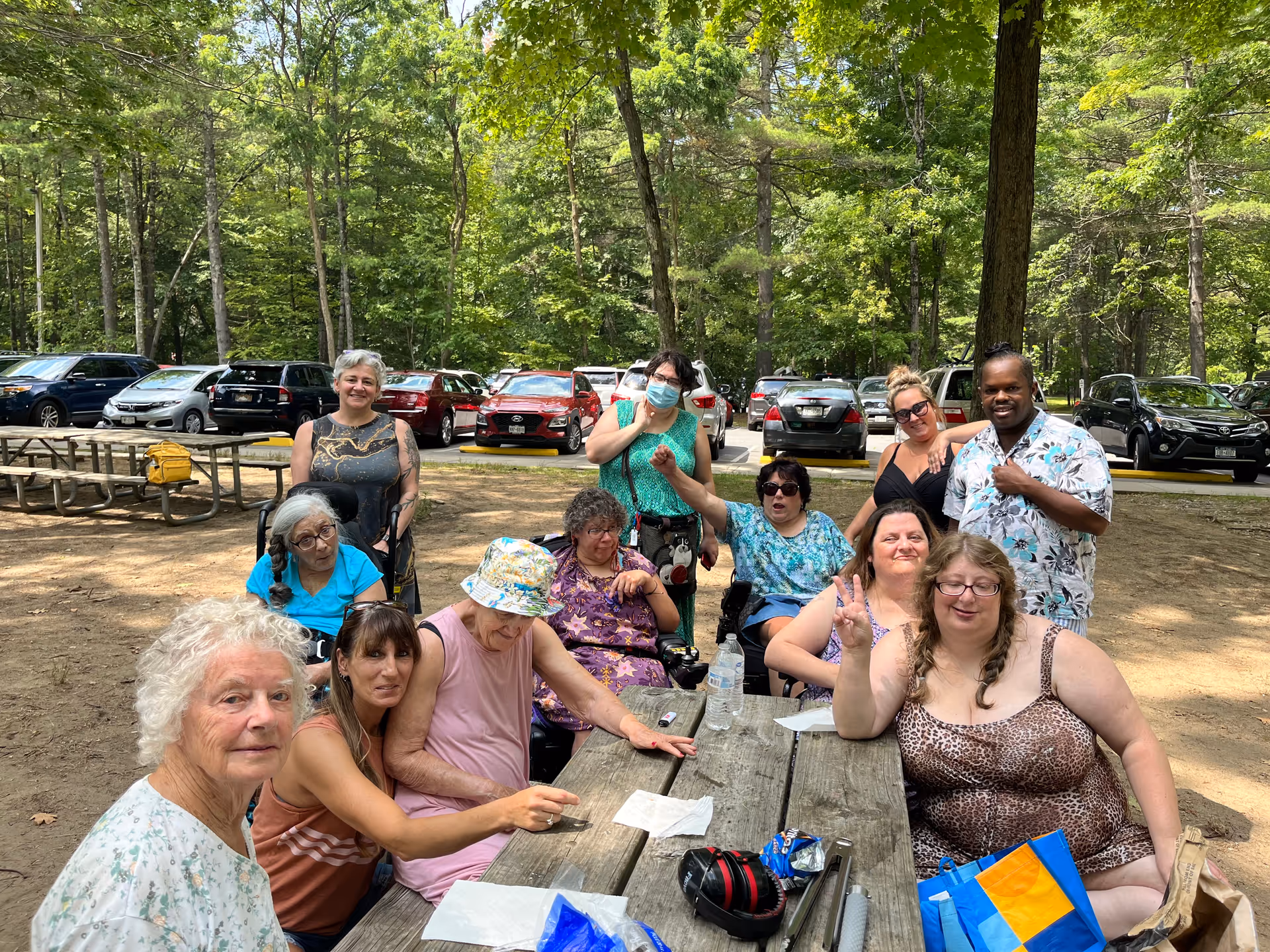 Group of seniors gathered outdoors around a wooden picnic table.