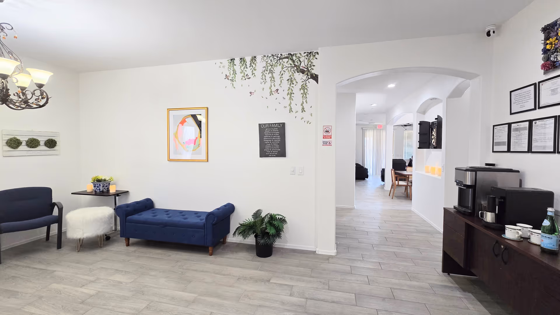 Bright, modern lounge with blue seating, a coffee station, plants, and an archway into a hallway.